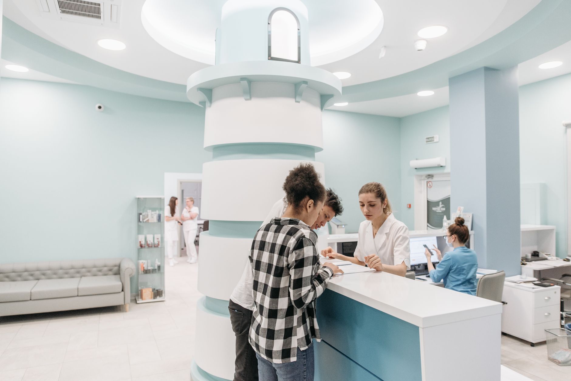 Two people look over paperwork with a staff member at a bright clinic reception desk